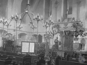 Интерьер синагоги, 1925. В центре бима, увенчанная короной и большим количеством светильников. На заднем плане виден резной деревянный шкаф Интерьер синагоги, 1925. В центре бима, увенчанная короной и большим количеством светильников. На заднем плане виден резной деревянный шкаф