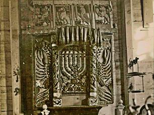 Fragment of aron-kodesh. In the center 2 lions hold Menora, against the background of a double-headed eagle. At the edges you can see the heads of this eagle, crowned with crowns.
At the top are animals with 4 species of plants, symbols of the festival of Sukkot: the bear with etrog, the eagle with lulav (palm leaves), the deer with adas (myrtle) and the lion with arava (willow) Fragment of aron-kodesh. In the center 2 lions hold Menora, against the background of a double-headed eagle. At the edges you can see the heads of this eagle, crowned with crowns.
At the top are animals with 4 species of plants, symbols of the festival of Sukkot: the bear with etrog, the eagle with lulav (palm leaves), the deer with adas (myrtle) and the lion with arava (willow)